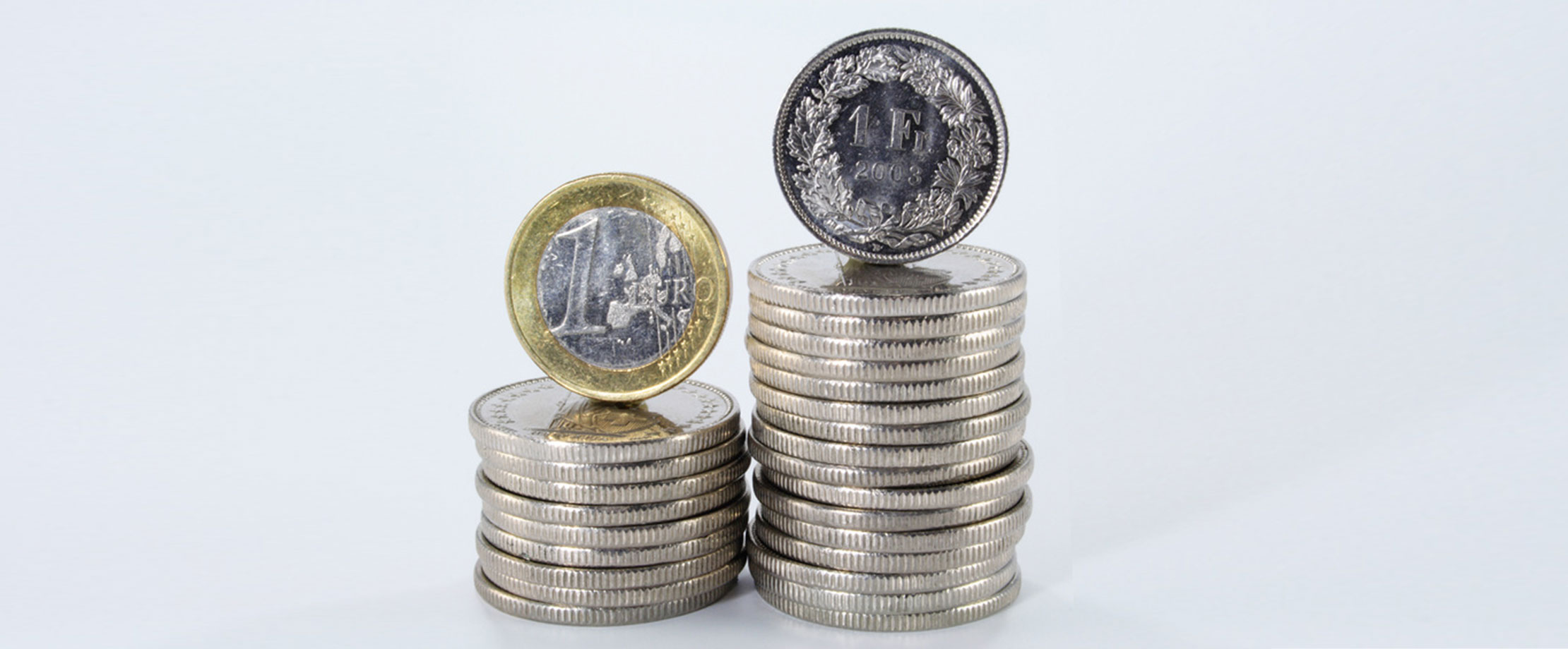 Ein Münzstapel Euros steht neben einem höheren Stapel Münzstapel von Schweizer Franken.  