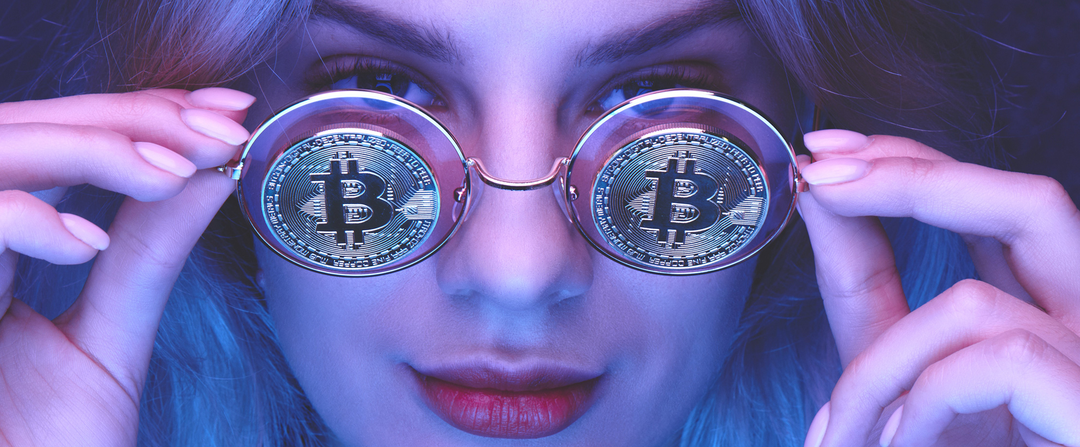 Das Gesicht einer jungen Frau wird von einem violetten Licht beleuchtet. Vor ihrem Gesicht hält sie eine runde Brille, auf deren Gläsern Bitcoin-Münzen abgebildet sind.
