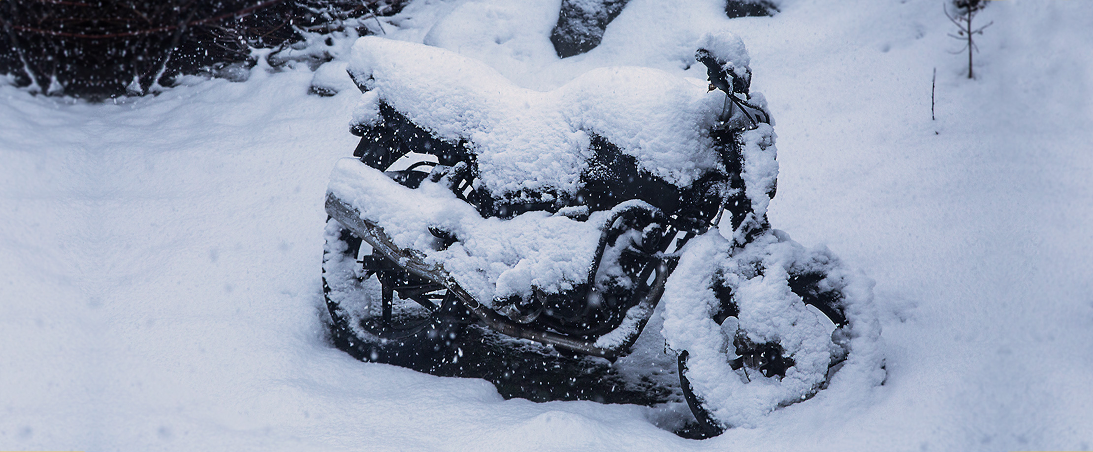 Ein schneebedecktes Motorrad steht im Wald. Der schwarze Lack ist unter der Schneemasse kaum zu sehen.