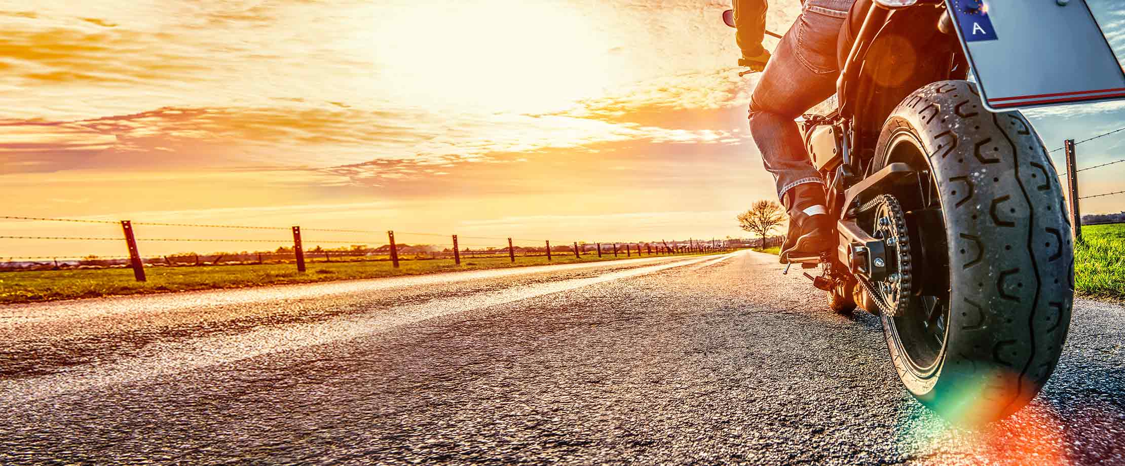 Ein Motorradfahrer fährt eine Feldstraße entlang dem Sonnenuntergang entgegen.